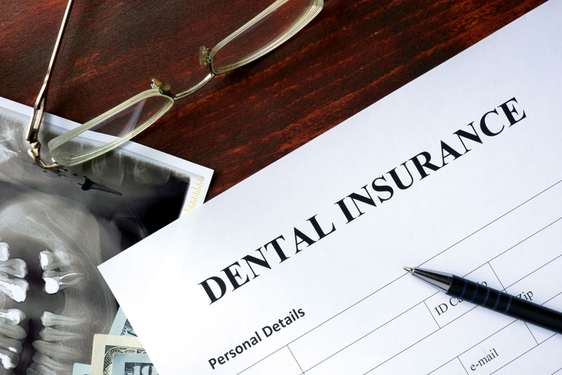Dental insurance claim form on a desk with a panoramic dental X-ray, reading glasses, and a pen