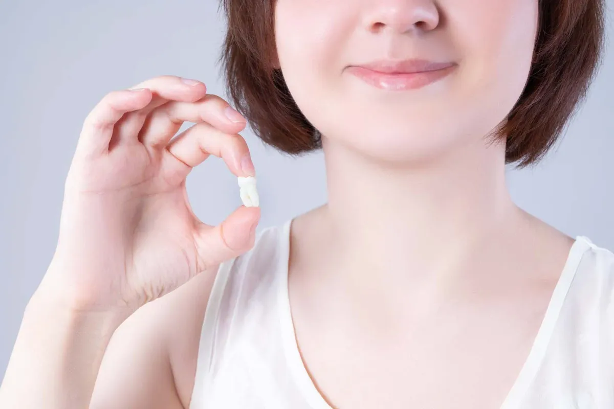 Smiling patient holding her extracted wisdom tooth after treatment